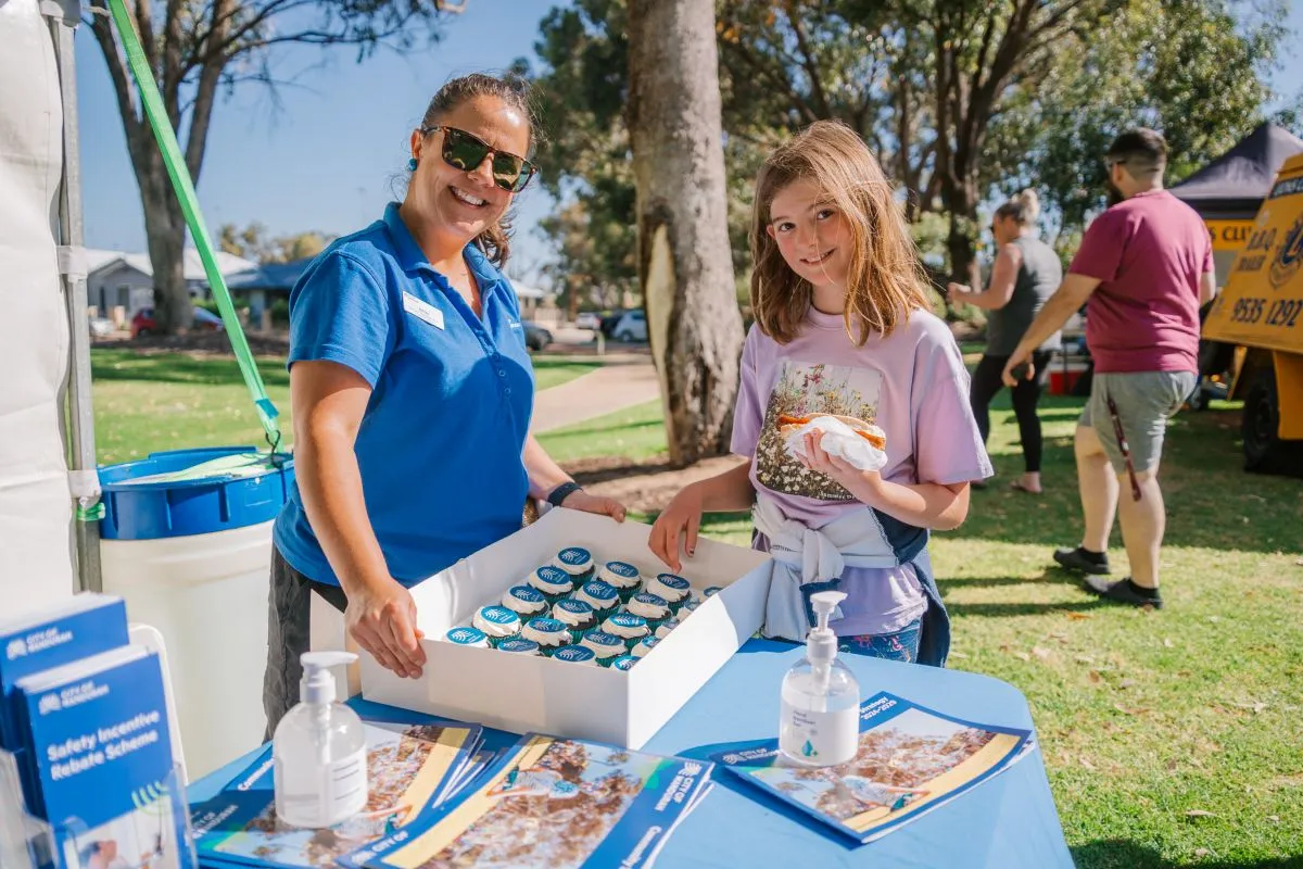 A Community Safety staff member handing out cupcakes to a young person at an outdoor event
